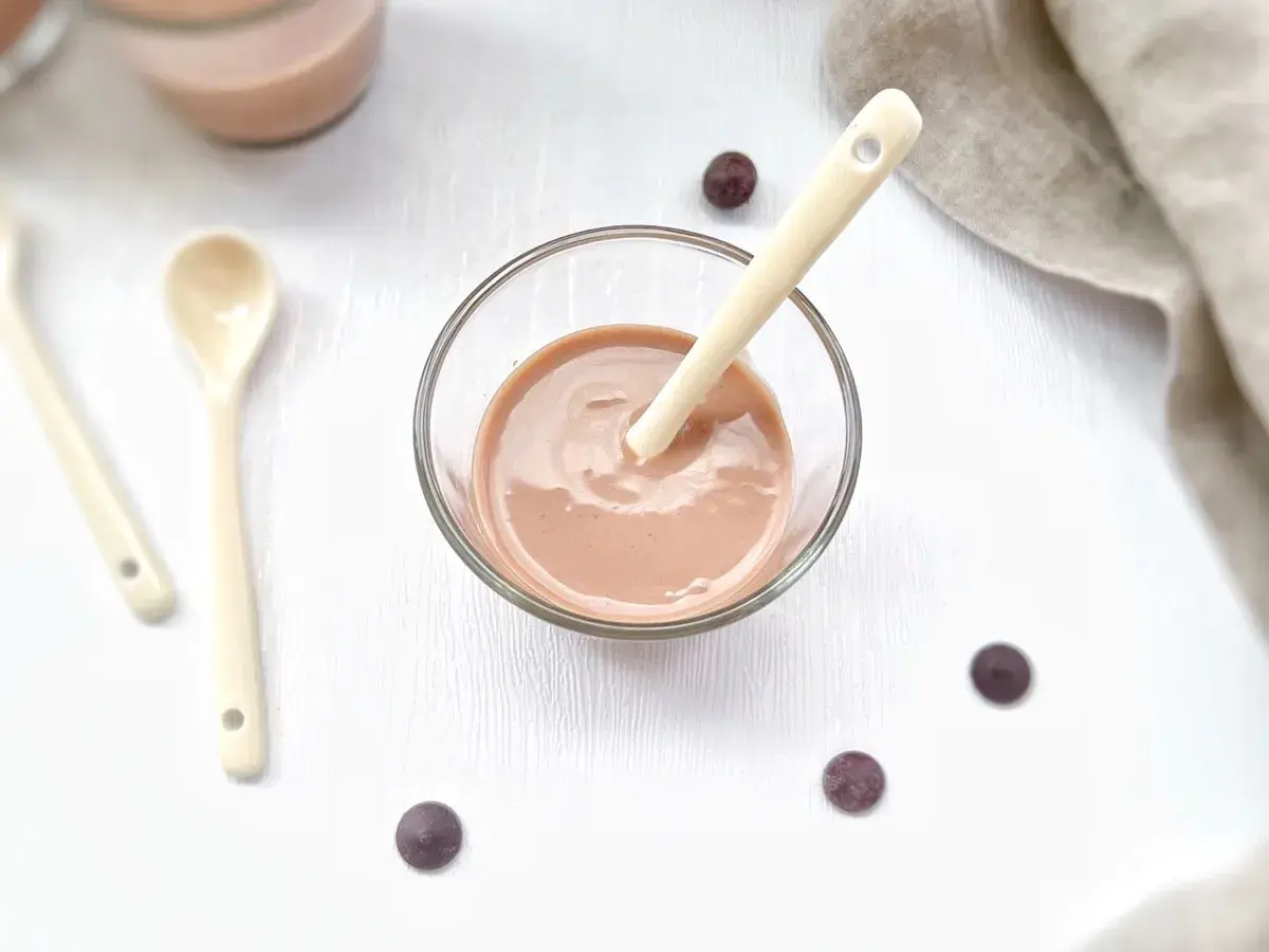 Un bol de ganache praliné onctueuse, prêt à être dégusté avec une cuillère. Quelques pépites de chocolat parsèment la table.