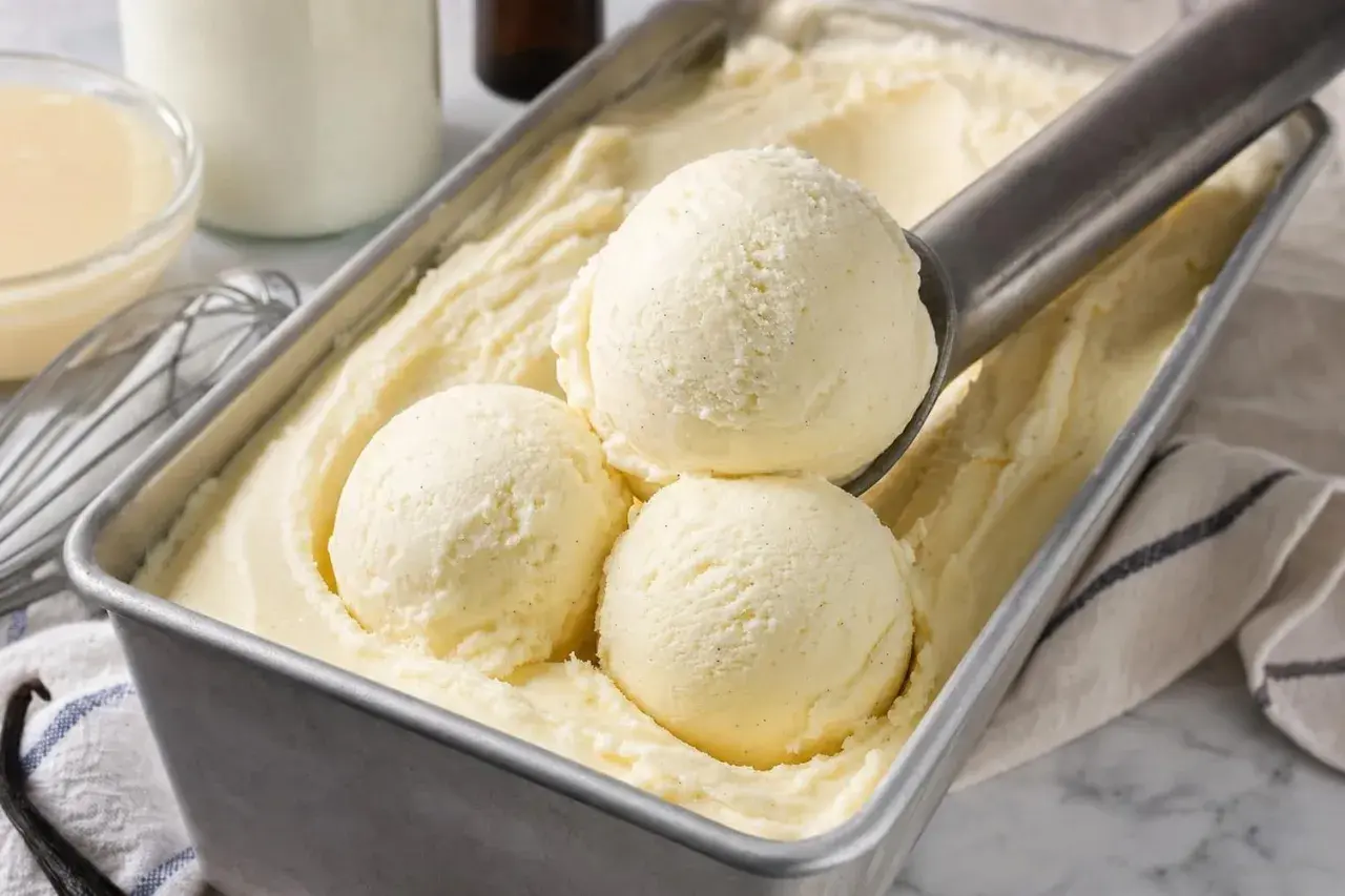 Une cuillère prélève des boules de glace à la vanille dans un bac. Une recette glace maison parfaite pour l'été.