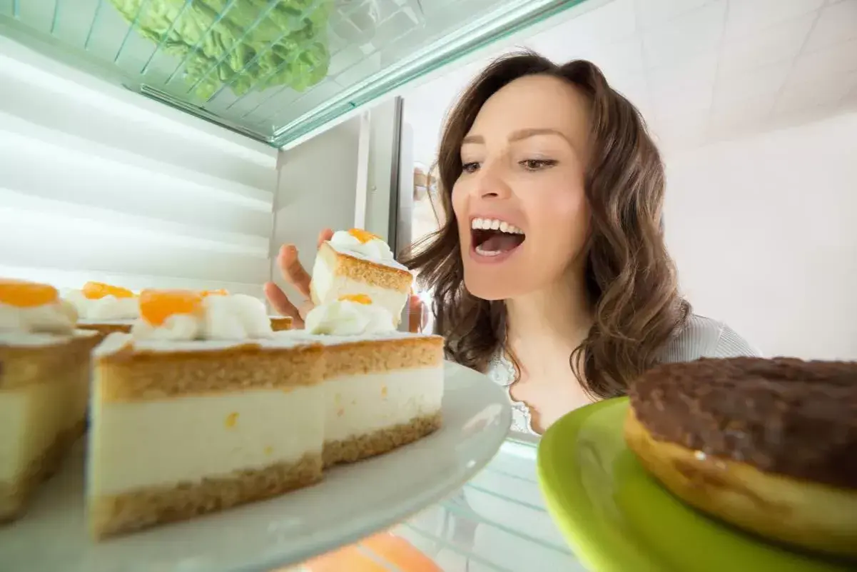 Une femme regarde des parts de gâteau à la crème pâtissière dans un réfrigérateur. Peut-on congeler une tarte à la crème pâtissière ?