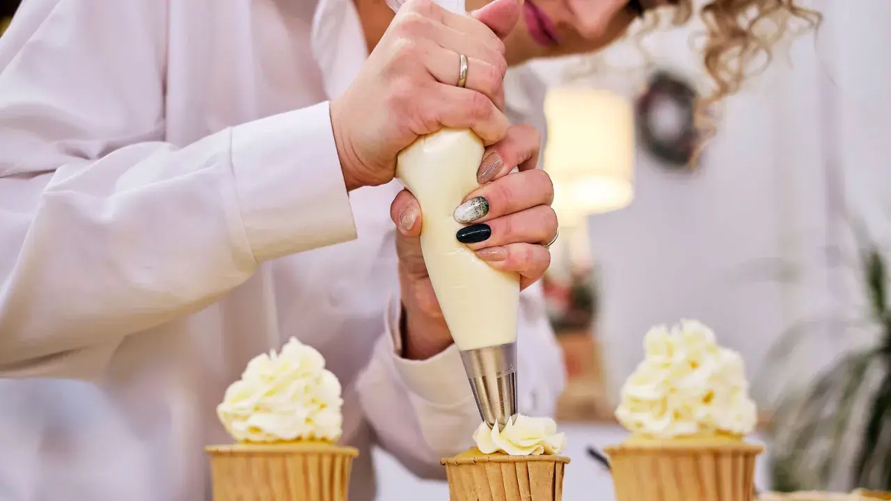 Pâtissière décorant des cupcakes avec une poche à douille. La crème est d'une belle couleur ivoire, parfaite pour savoir quel colorant pour chantilly mascarpone utiliser.
