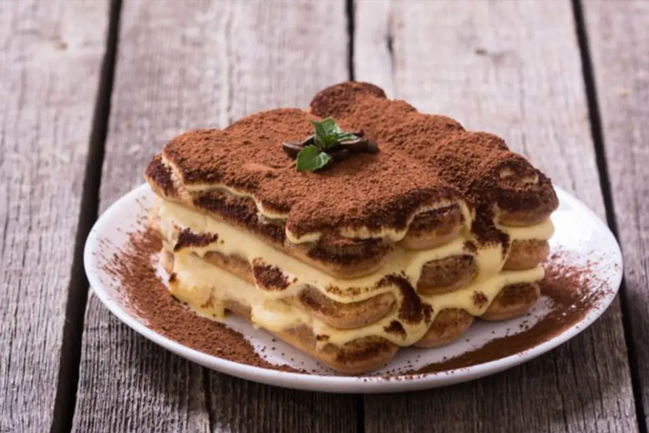 Un délicieux tiramisu, dont l'origine italienne est évidente, saupoudré de cacao, sur une assiette blanche.