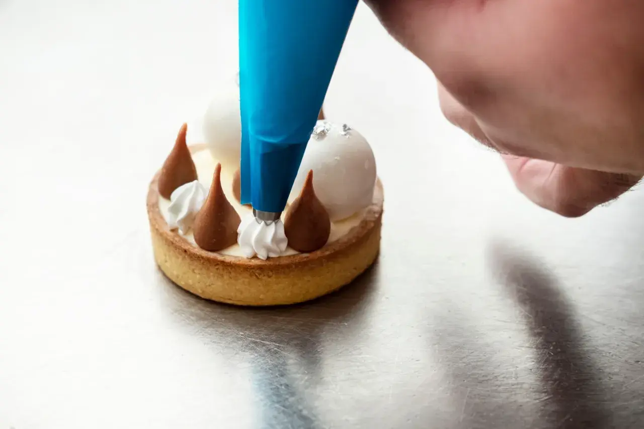 Un chef utilise une poche à douille bleue pour le pochage d'une crème sur un petit gâteau.