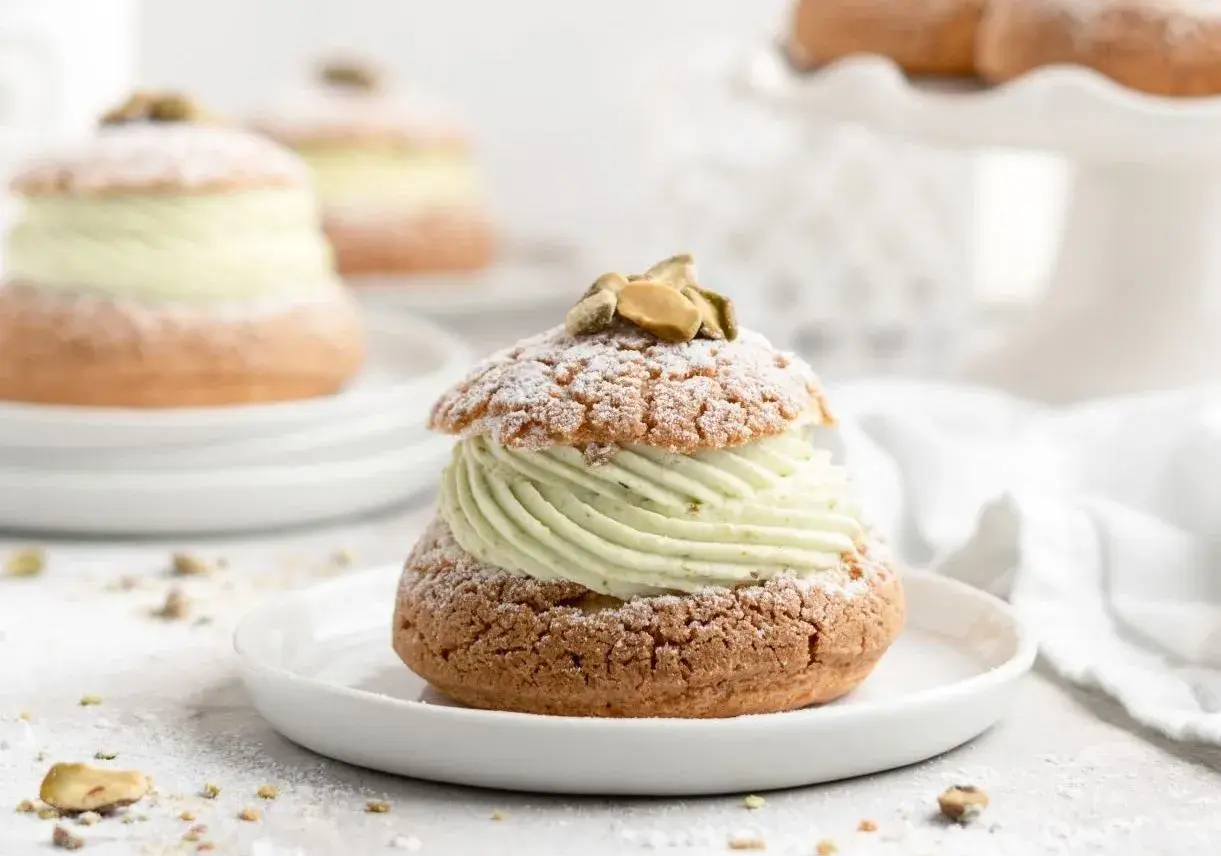 Un délice aérien : une religieuse garnie d'une crème onctueuse à la pistache, saupoudrée de sucre glace et décorée de pistaches.