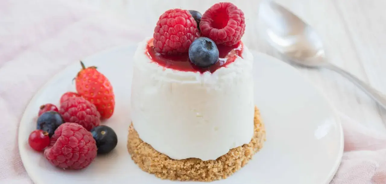 Délicieux dessert sans cuisson, un petit gâteau crémeux garni de fruits rouges frais et d'un coulis.