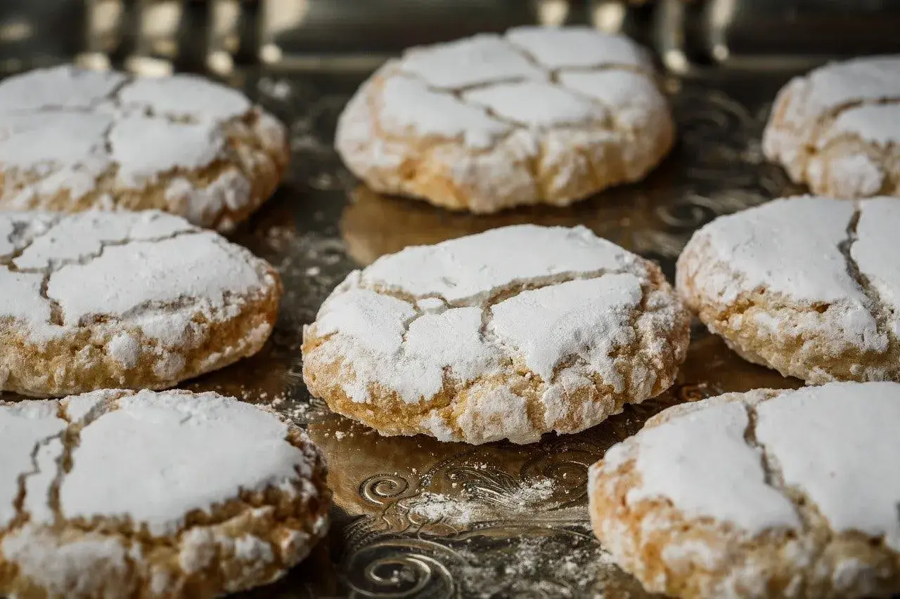 Biscuits craquelés saupoudrés de sucre glace, parfaits pour accompagner votre café. Une idée pour comment faire de la poudre d'amande maison.