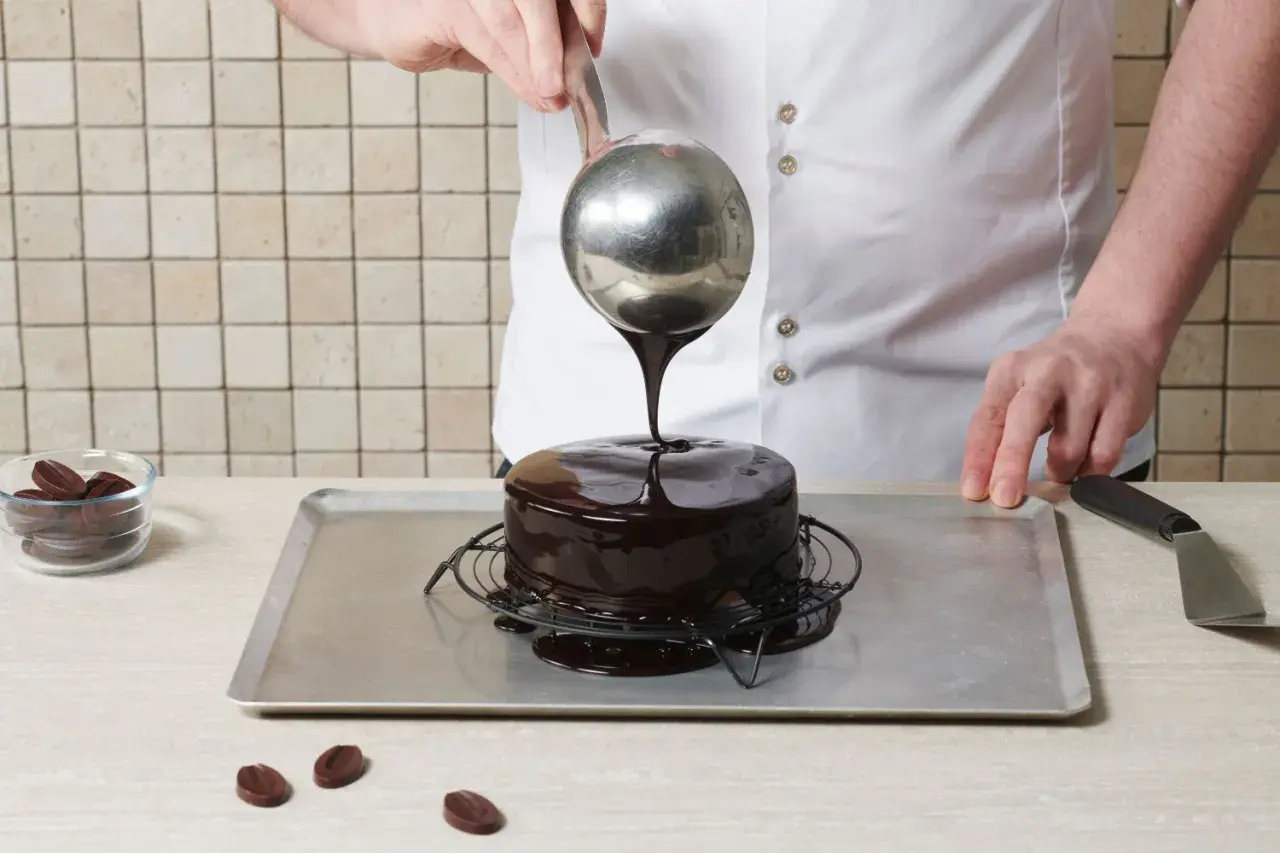 Un chef verse un glaçage au chocolat brillant sur un gâteau, créant le meilleur glaçage pour décorer un gâteau.