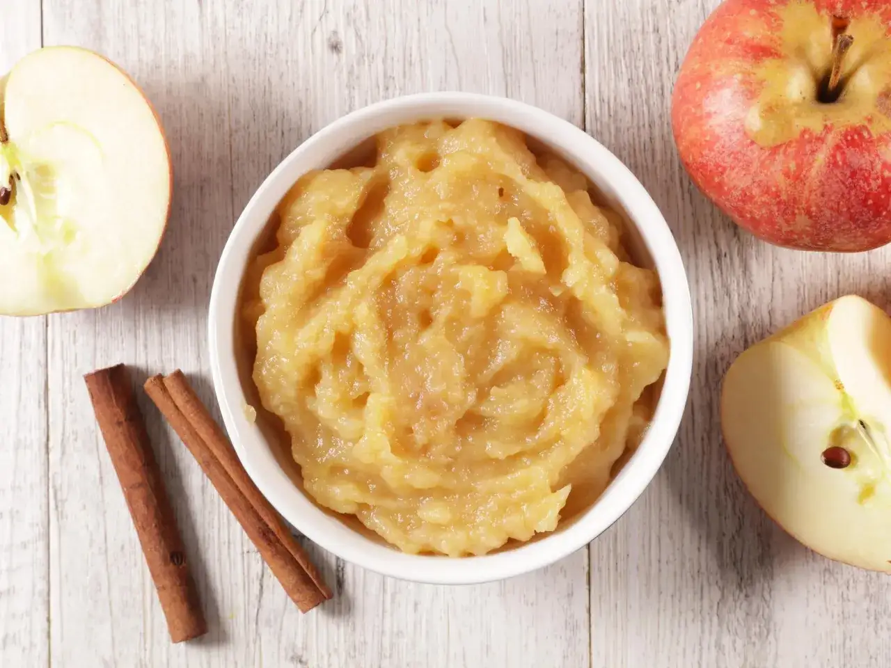 Compote de pommes dans un bol blanc, avec des pommes coupées et des bâtons de cannelle. Une excellente alternative pour remplacer oeuf par compote dans vos recettes.