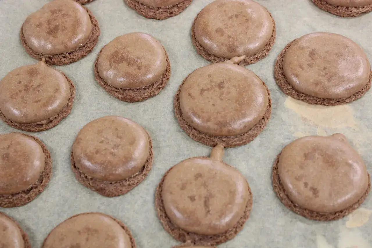 Des macarons au chocolat sur une plaque. Certains ont des pieds craquelés, expliquant pourquoi mes macarons craquent.