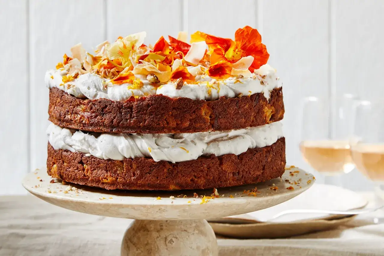 Gâteau healthy à deux étages, garni de crème fouettée, de copeaux de noix de coco et de fleurs comestibles.