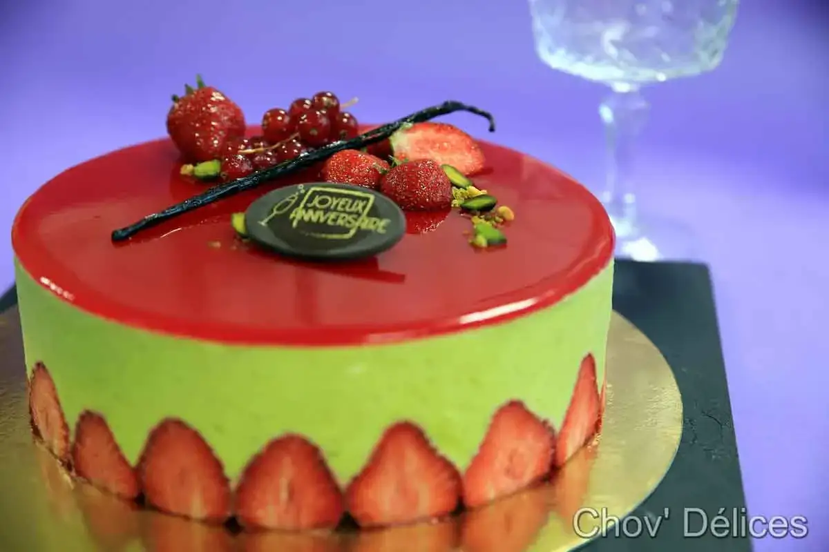 Gâteau vert pistache avec glaçage rouge, décoré de fraises, groseilles, pistaches et une gousse de vanille. Une délicieuse décoration fraisier pour un anniversaire.