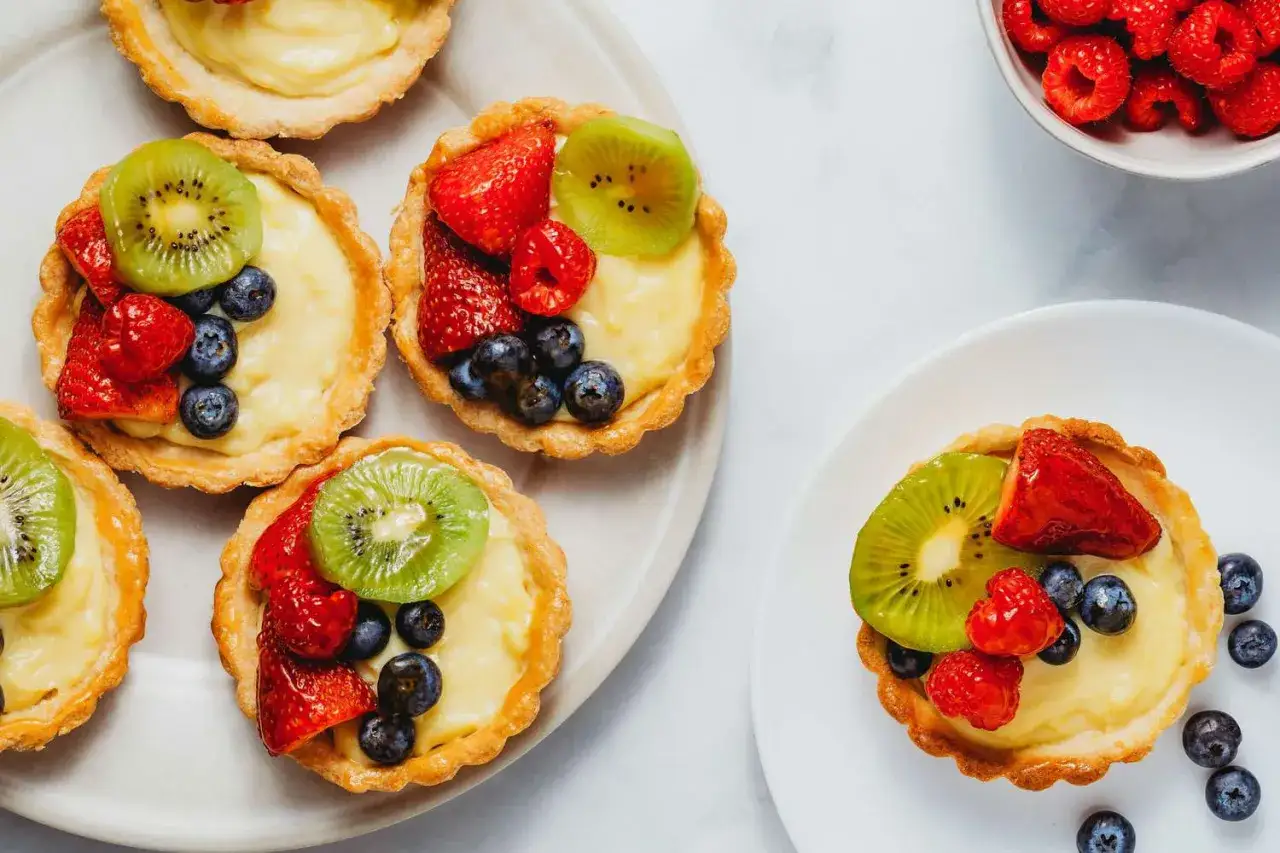 Des tartelettes garnies de cr&egrave;me p&acirc;tissi&egrave;re, d&eacute;cor&eacute;es de fraises, myrtilles, framboises et kiwi. Id&eacute;al pour savoir que mettre sur un fond de tarte aux fruits.