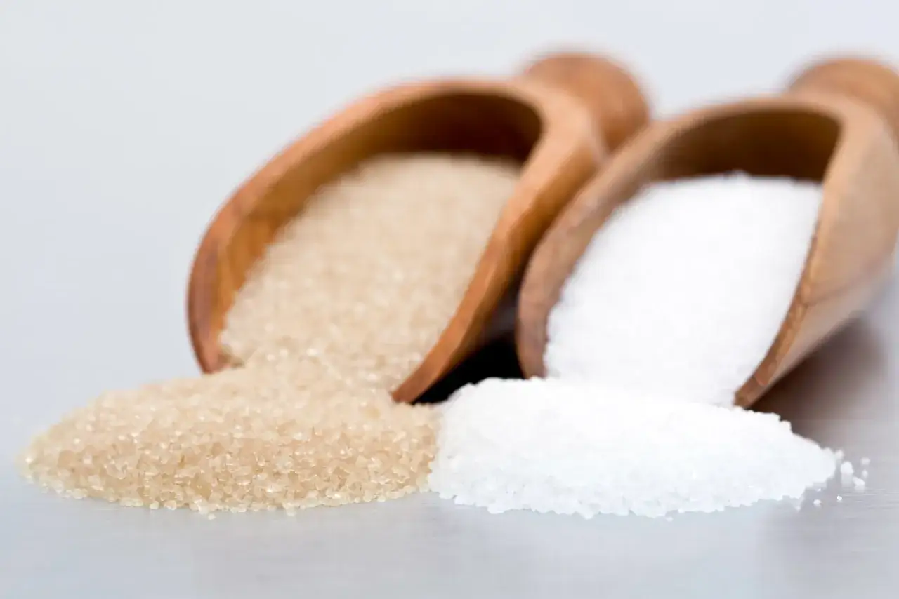 Deux cuillères en bois contiennent différents types de sucre en pâtisserie : du sucre blanc fin et du sucre roux.