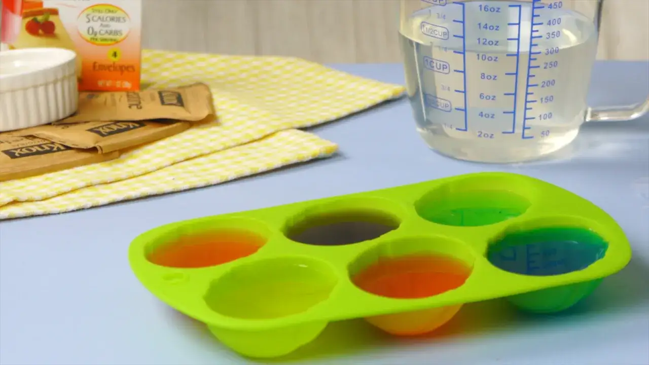 Pr&eacute;paration de gelatine en poudre comment l'utiliser : des sachets Knox, un moule en silicone rempli de gel&eacute;es color&eacute;es et un verre doseur.