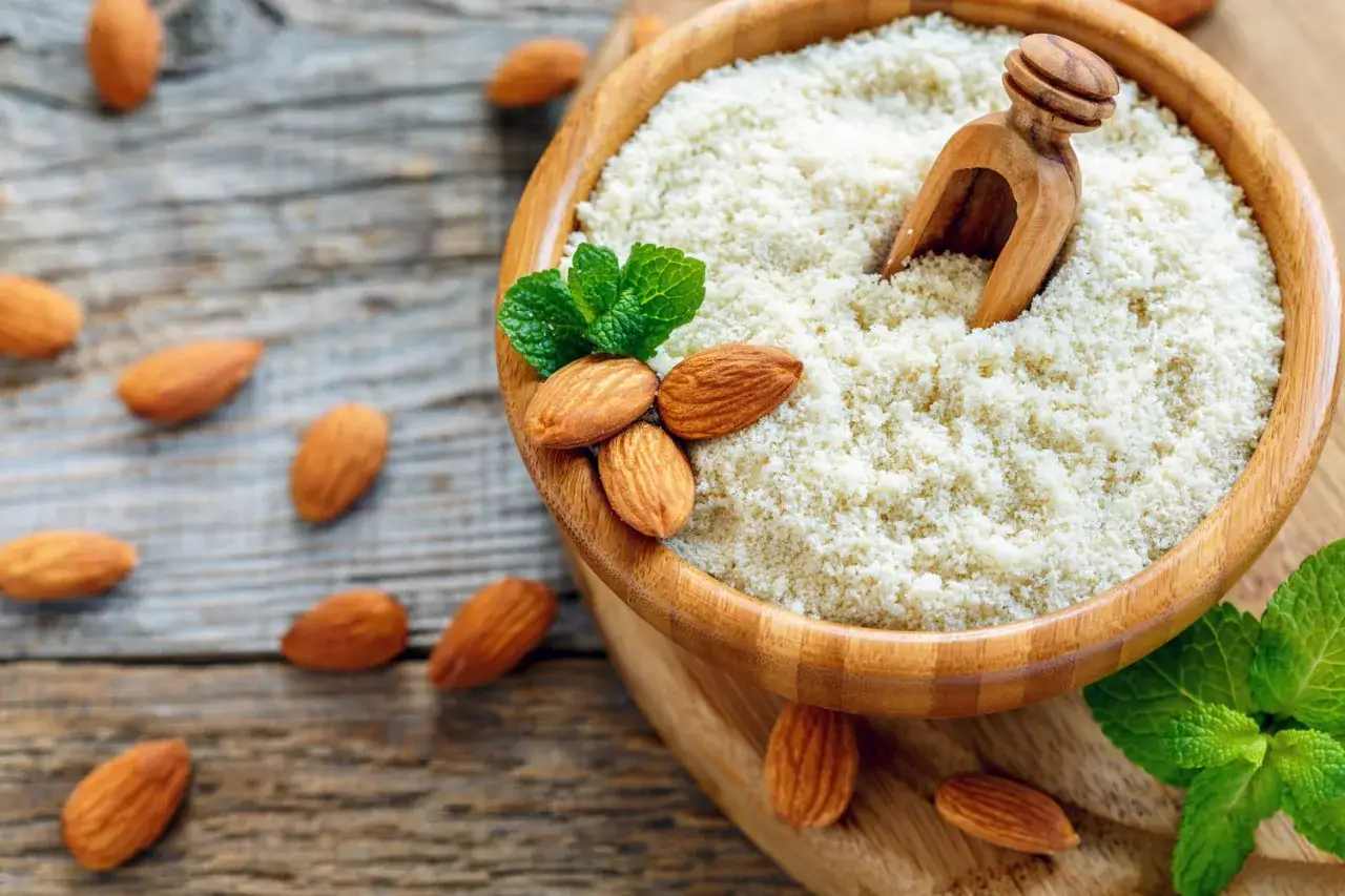 Un bol en bois rempli de farine d'amande ou poudre d'amande, avec des amandes entières et des feuilles de menthe.