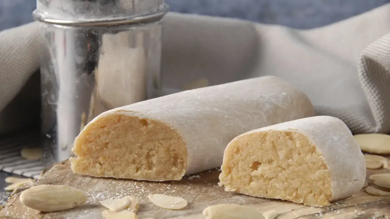 Pâte d'amande pour recouvrir un gâteau, saupoudrée de sucre glace, avec des amandes effilées autour.