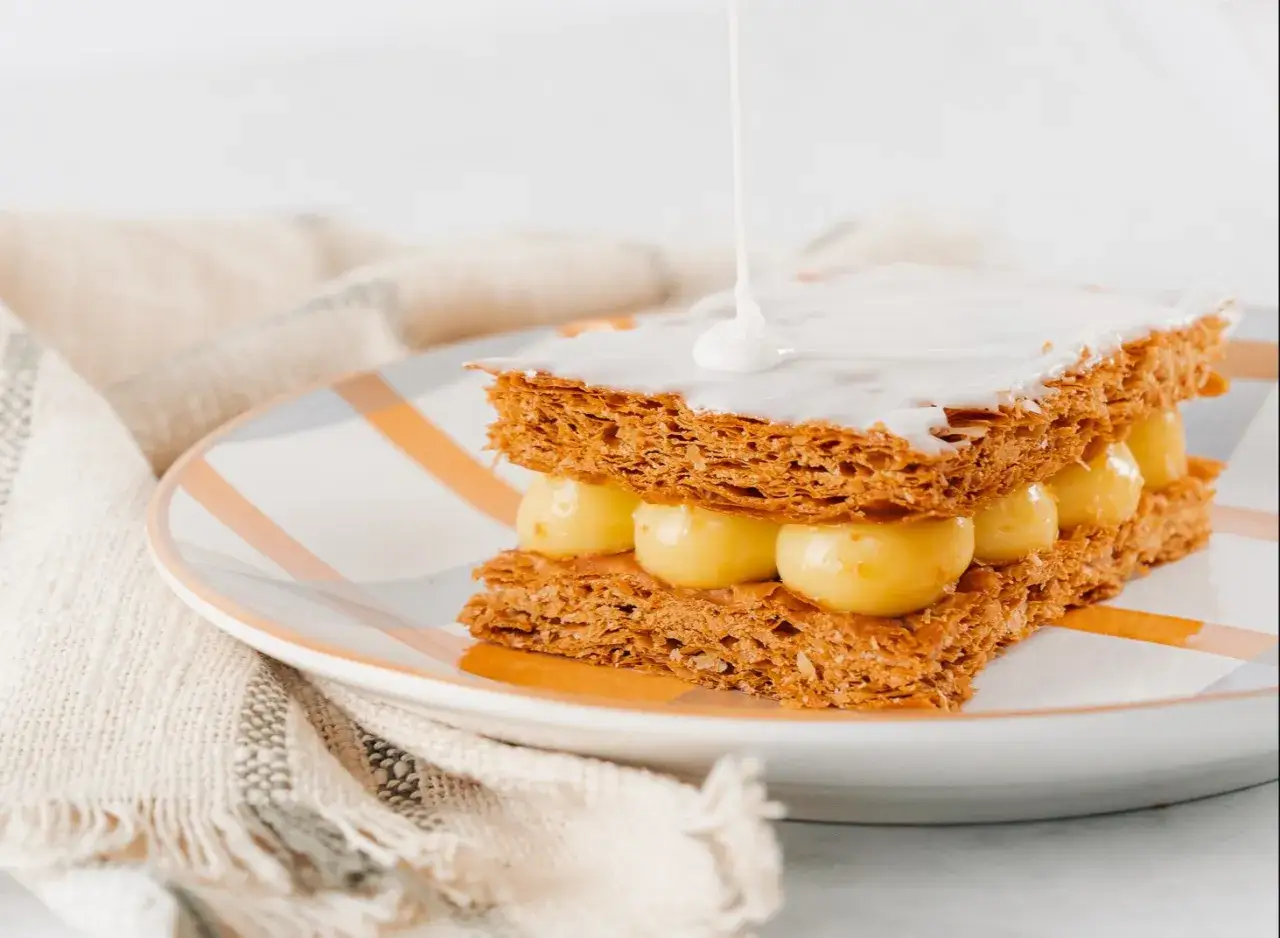 Un millefeuille croustillant avec une crème pâtissière onctueuse, recouvert d'un glaçage millefeuille blanc et lisse.