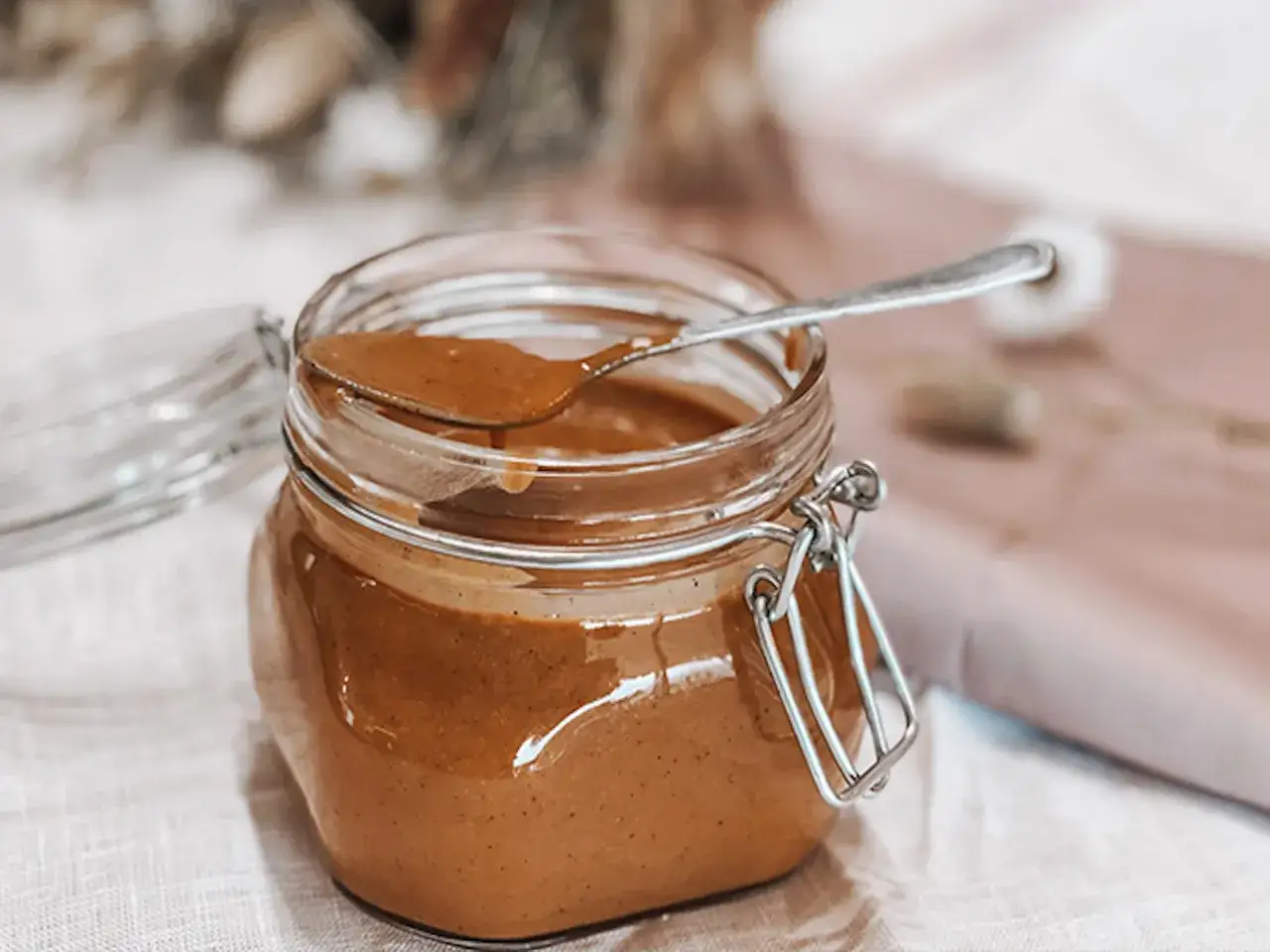 Un pot en verre ouvert contient une délicieuse préparation de praliné maison. Une cuillère y est posée, prête à être utilisée.