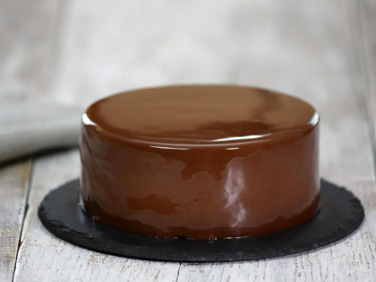 Gâteau rond avec un glaçage chocolat miroir brillant, posé sur une assiette en ardoise.