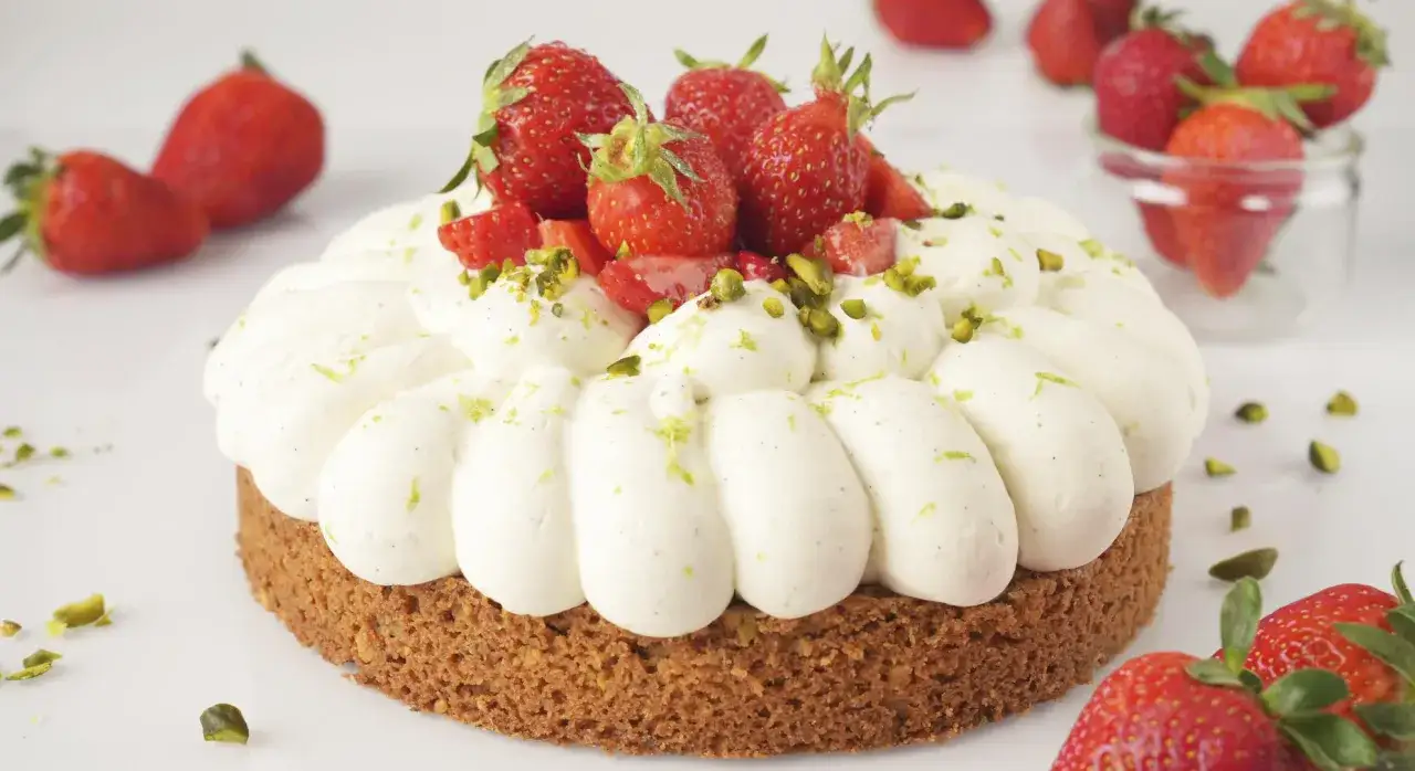 Gâteau rond garni de crème fouettée, fraises fraîches et éclats de pistaches. Une délicieuse ganache fraise se cache sous cette garniture.