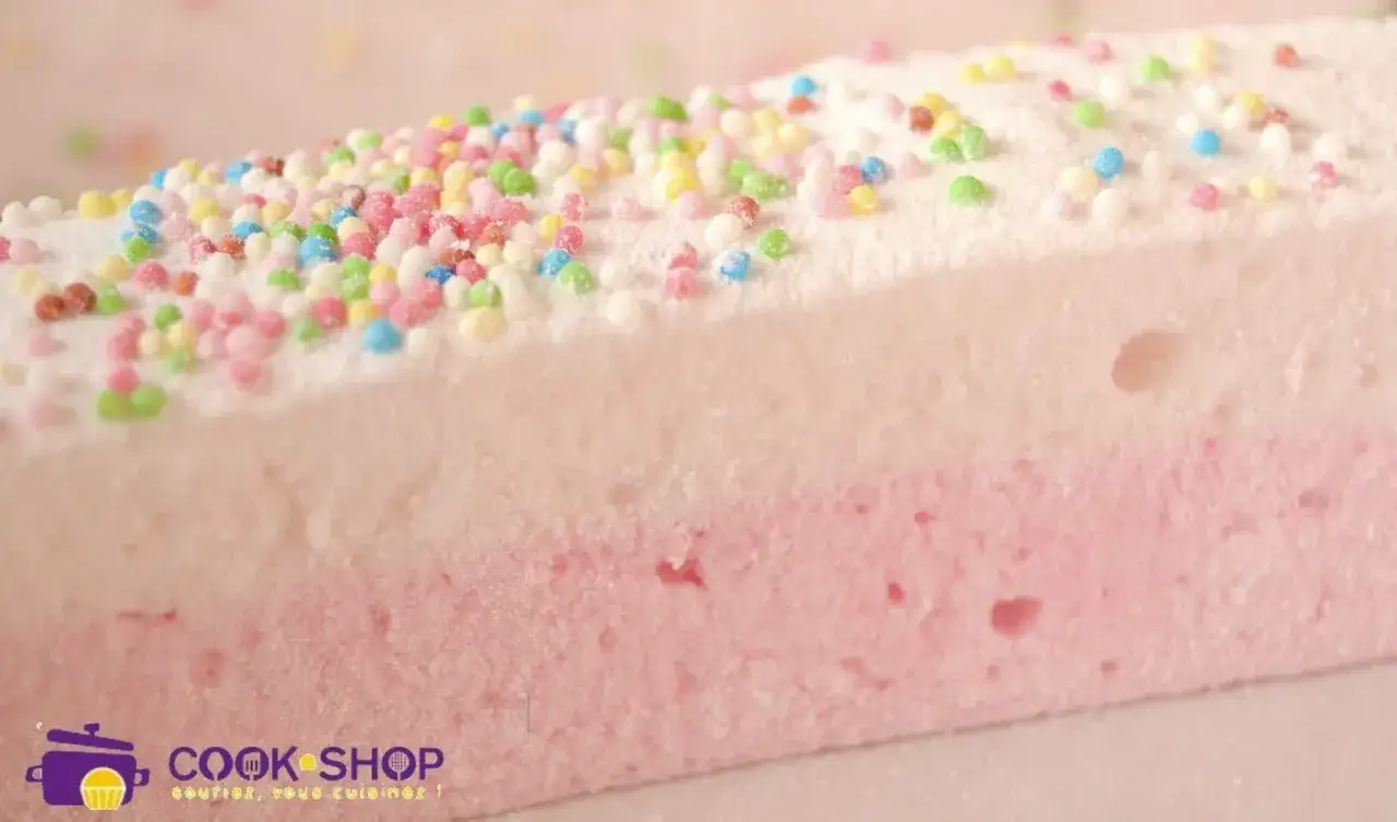 Un gros plan sur un ingrédient guimauve bicolore, blanc et rose, saupoudré de vermicelles colorés.