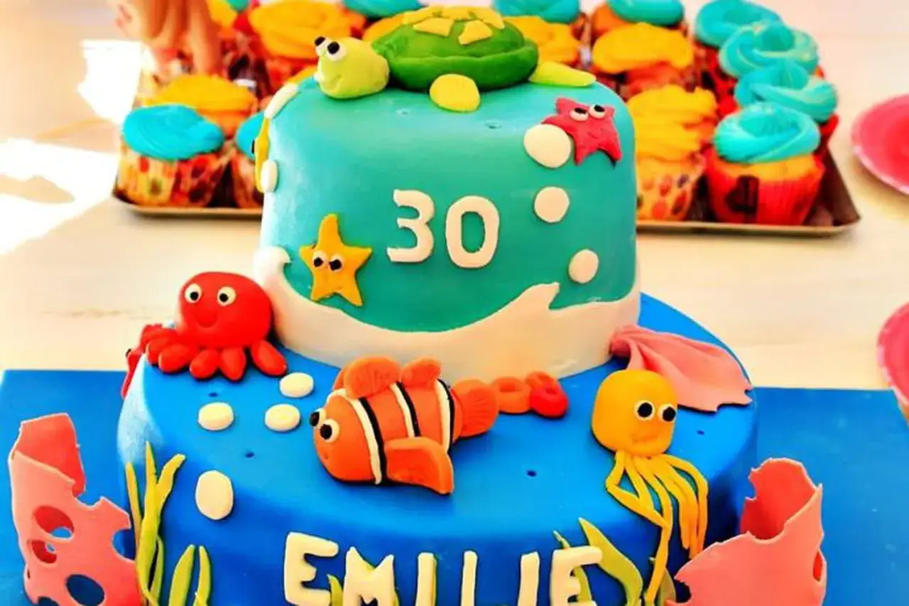 Gâteau d'anniversaire pâte à sucre sur le thème de la mer, avec une tortue, des étoiles de mer, un poisson-clown et des poulpes. Le chiffre 30 est visible.