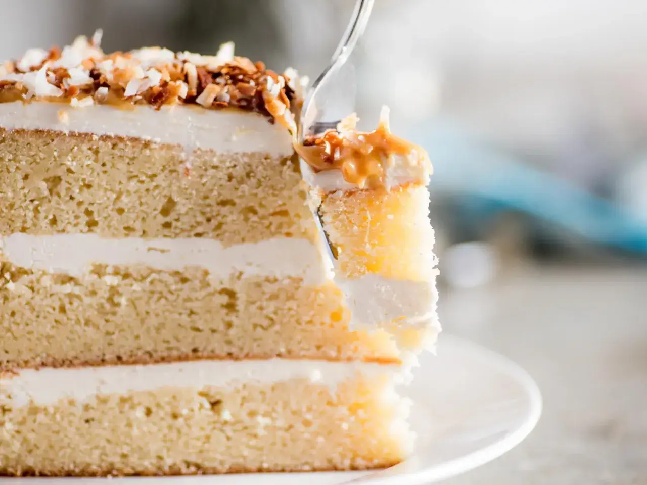 Une part de gâteau moelleux aux couches de crème noix de coco, garnie de noix de coco grillée et de caramel.
