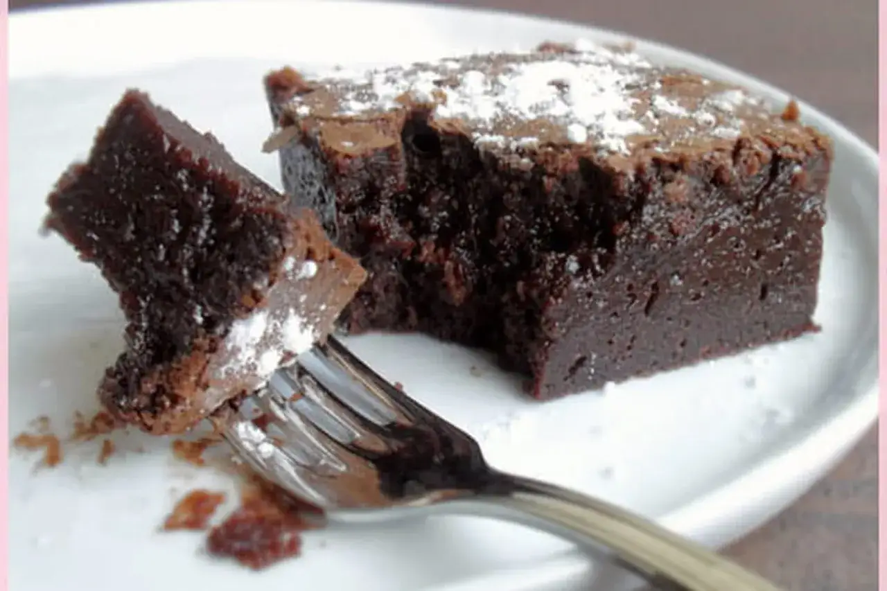 Un morceau de délicieux mud cake au chocolat, saupoudré de sucre glace, est prêt à être dégusté avec une fourchette.