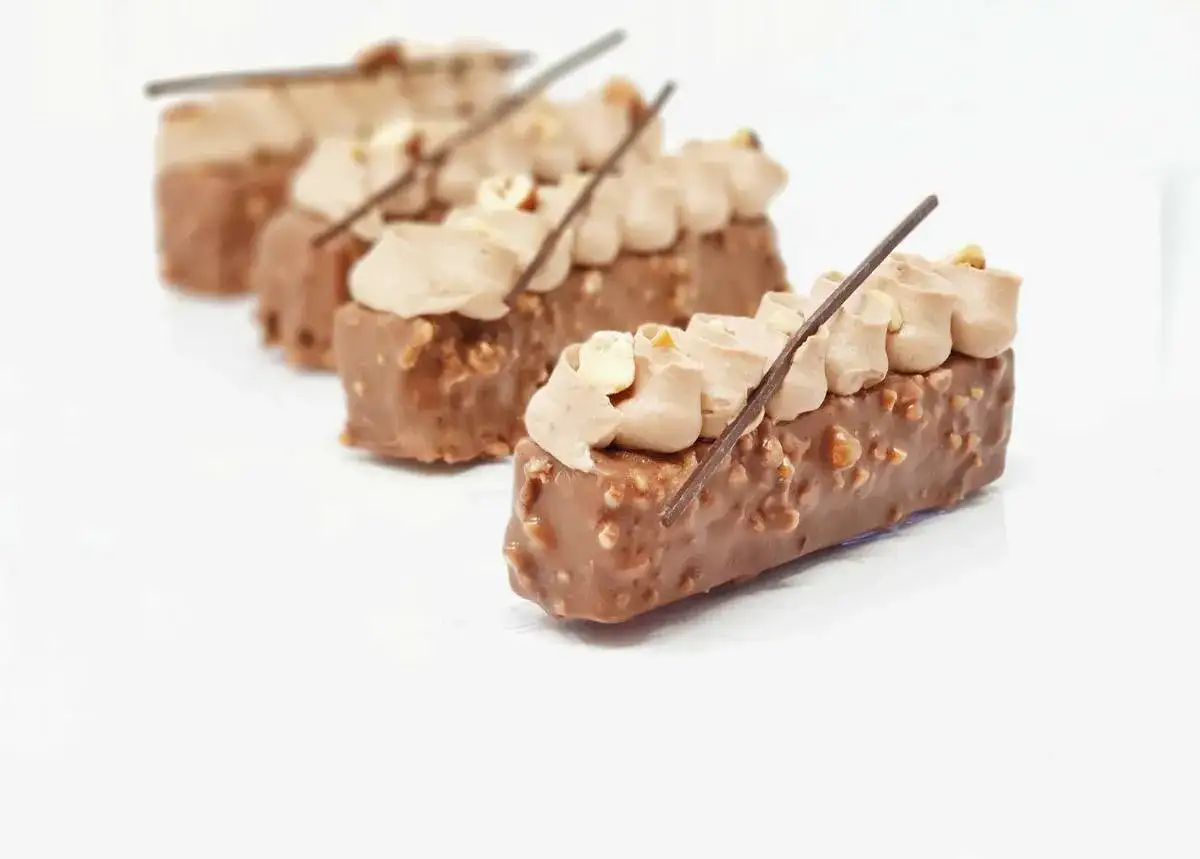 Petits gâteaux rectangulaires enrobés d'un glaçage rocher croquant, garnis de crème au chocolat et décorés d'une bâtonnet de chocolat et de noisettes.
