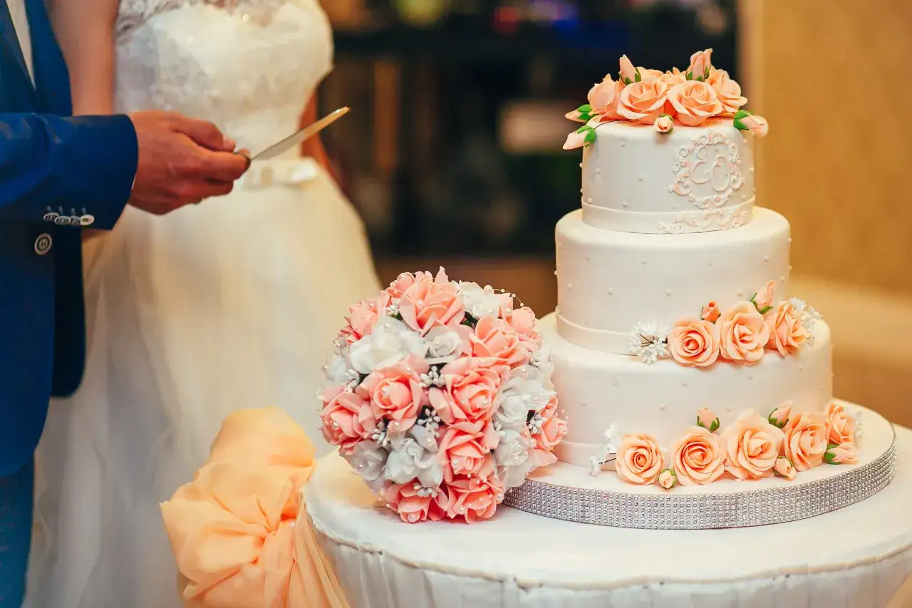 Un magnifique layer cake 2 étages orné de roses pêche et d'un bouquet assorti, prêt à être coupé par les mariés.