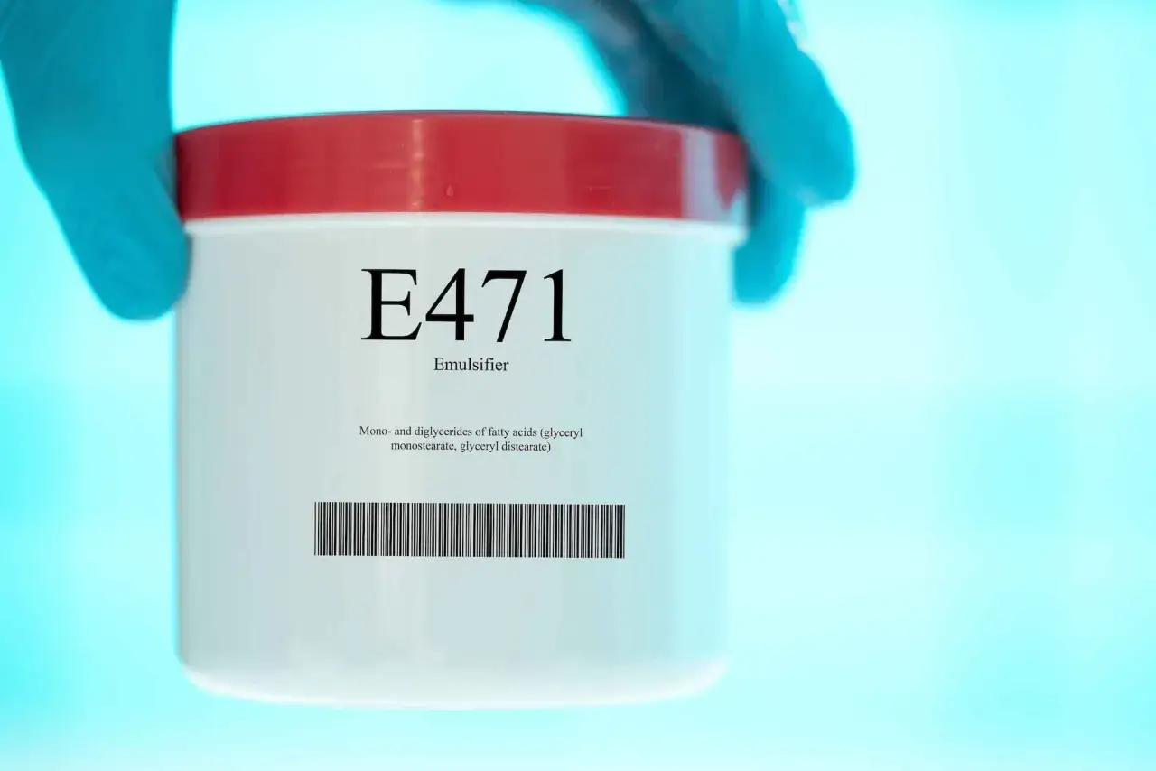 Main de laboratoire tenant un pot étiqueté E471, émulsifiant, monostéarate de glycérol.