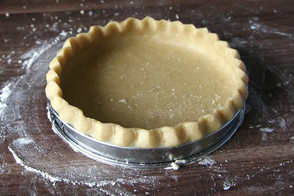 Pâte brisée crue dans un moule à tarte, prête à être cuite. Attention à la péremption pâte brisée si vous utilisez une pâte du commerce.