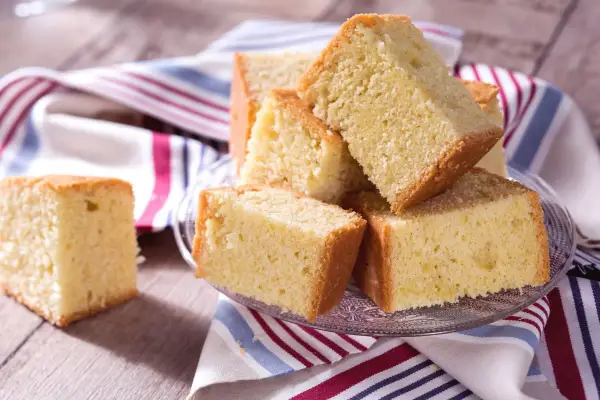 Tranches de madeira cake dorées et moelleuses, empilées sur une assiette en verre, avec une serviette rayée.