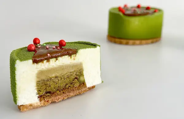 Entremet pistache aux couches délicates de mousse blanche, de crémeux et de biscuit croustillant, décoré de fruits rouges.